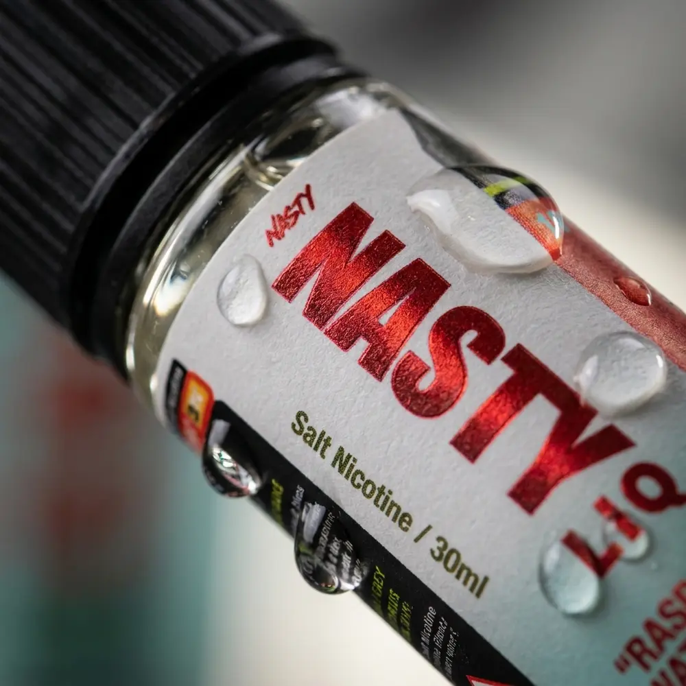 Close-up do rótulo e bocal do Nasty Juice Salt Raspberry Watermelon com gotas e reflexos detalhados - Vapor Gringo