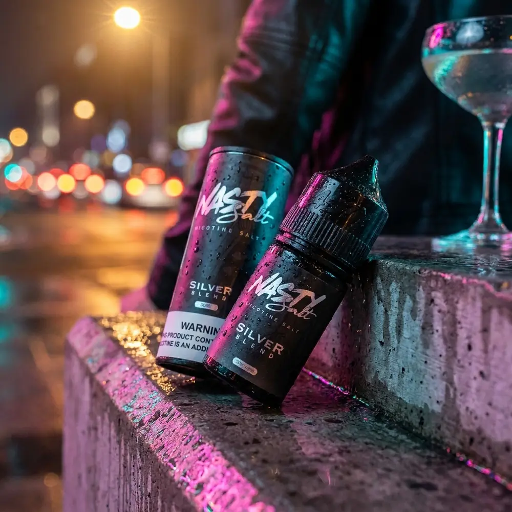Frasco Nasty Juice Salt Silver Blend num parapeito molhado com reflexos de neon urbano ao fundo - Vapor Gringo