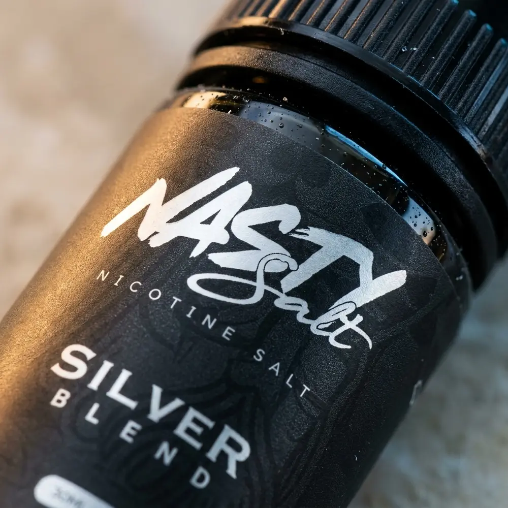 Detalhe macro do rótulo e bico do Nasty Juice Salt Silver Blend com gotas e reflexos realistas - Vapor Gringo