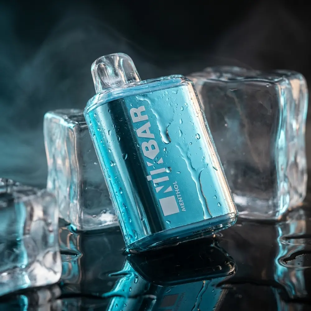 Pod descartavel NikBar 15.000 puffs menthol apoiado em bloco de gelo sobre acrilico molhado, luz azul fria - Vapor Gringo