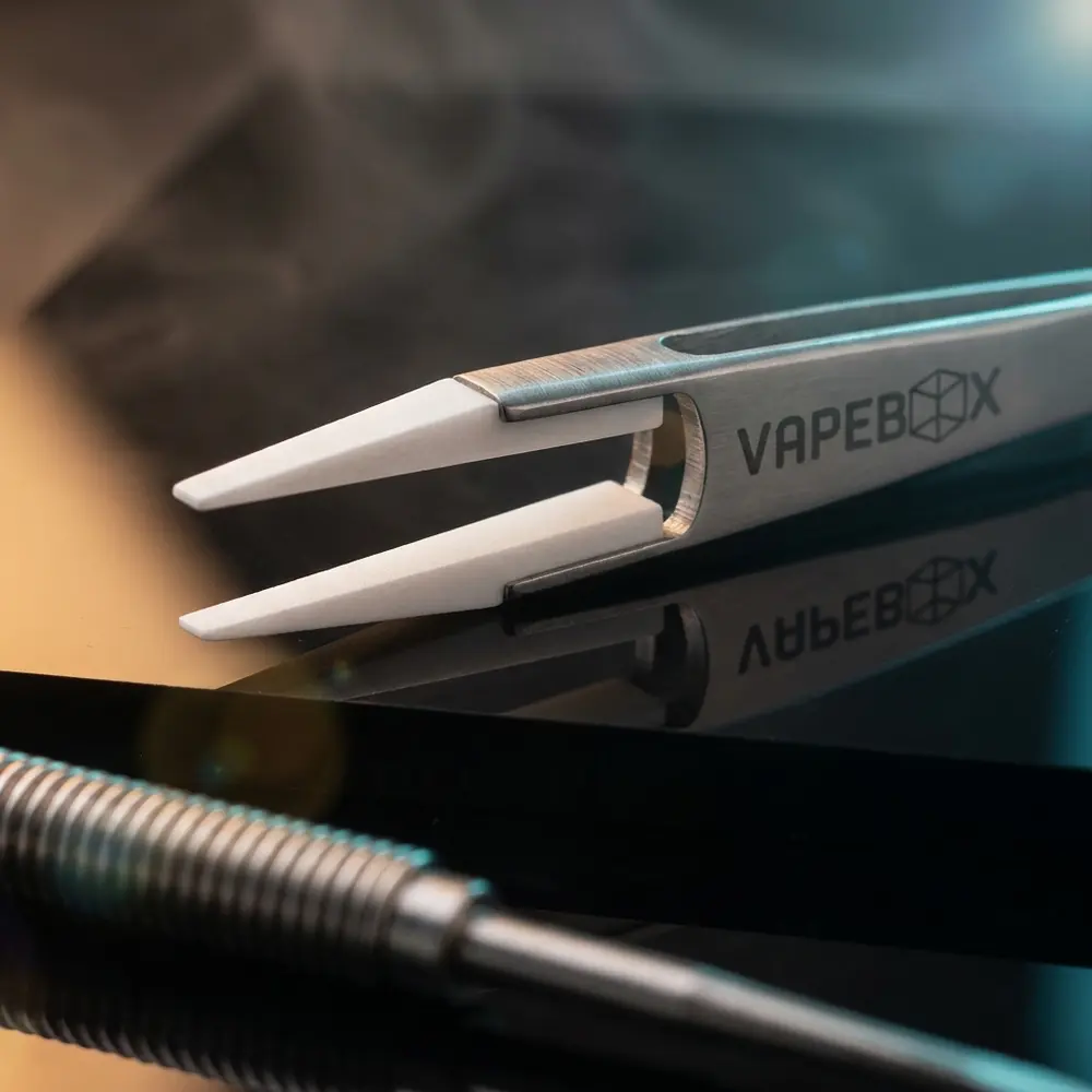 Pinça de cerâmica Vapebox diagonada sobre acrílico preto com luzes quentes e frias e reflexos - Vapor Gringo