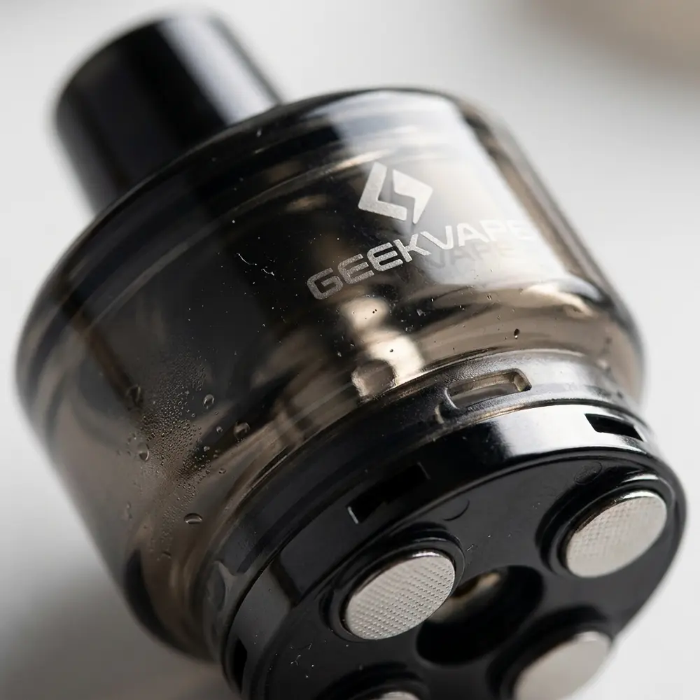 Close-up macro do pod Crown M Uwell mostrando transparencia PCTG, contatos metalicos e pequenas gotas de condensacao - Vapor Gringo