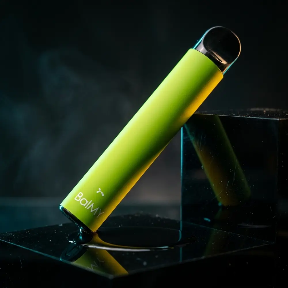 Pod Descartável Balmy Mango sobre plinto acrílico escuro com reflexos dramáticos e luz dourada - Vapor Gringo