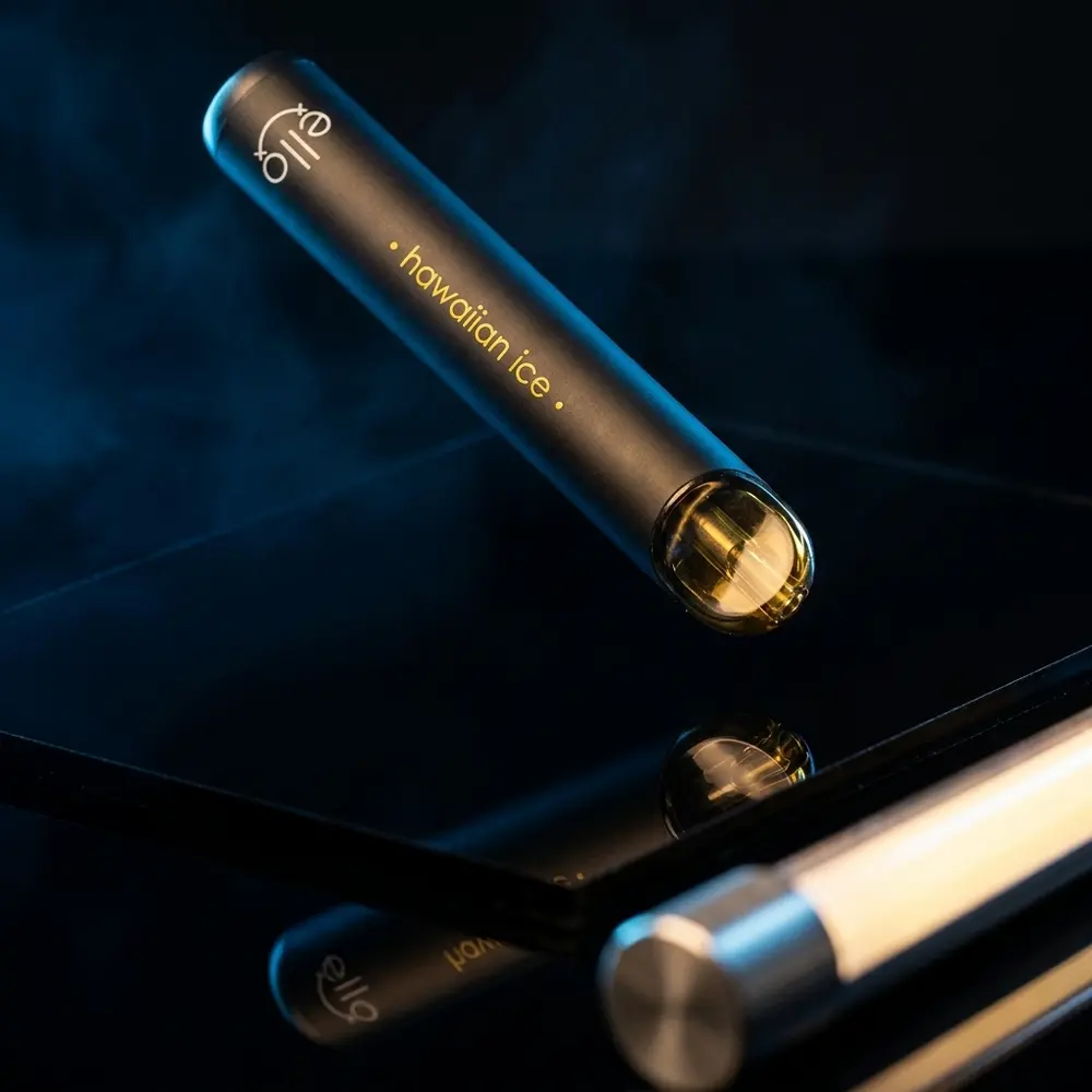 Pod descartavel Blvk Ello Hawaiian Ice suspenso sobre base acrilica preta, reflexos e fumaça sutil - Vapor Gringo