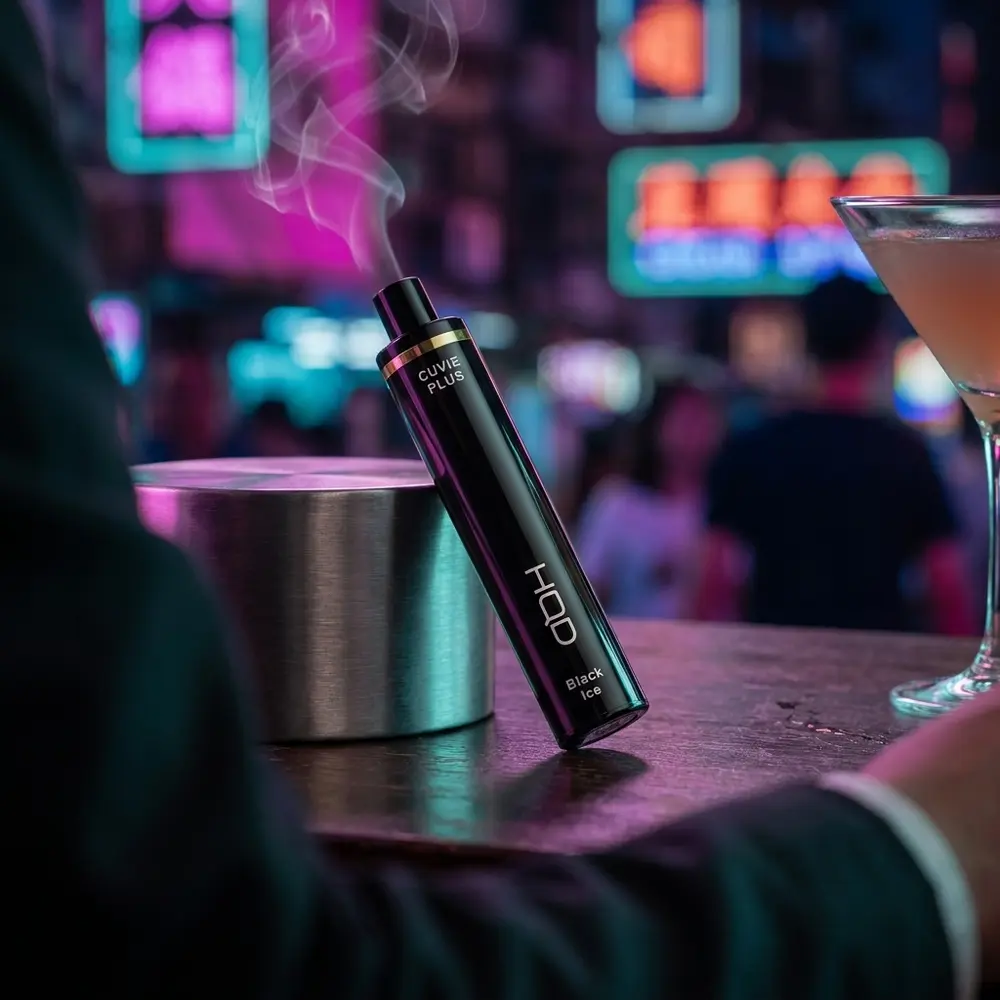 Pod HQD Cuvie Plus apoiado em balcão urbano com neon desfocado ao fundo e reflexos coloridos - Vapor Gringo