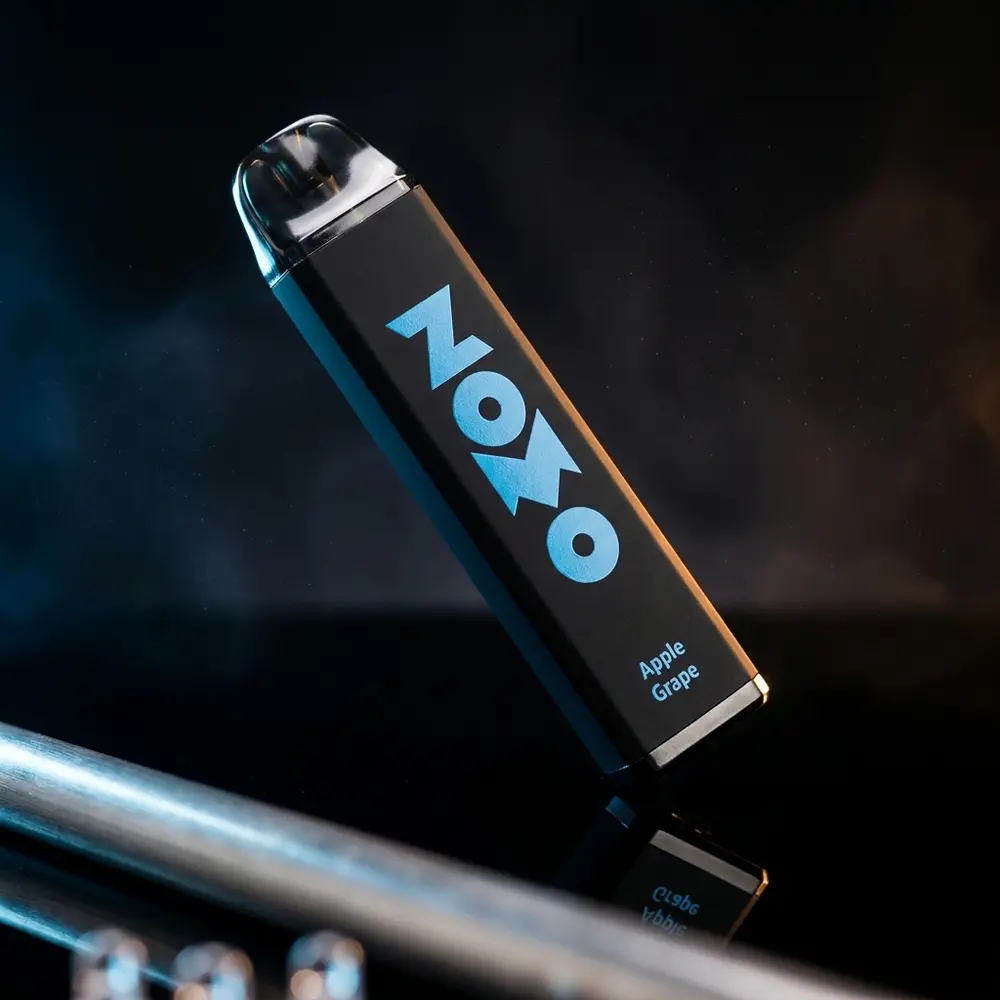 Pod descartável Zomo Party Apple Grape em close sobre acrílico preto com reflexos azuis e âmbar - Vapor Gringo