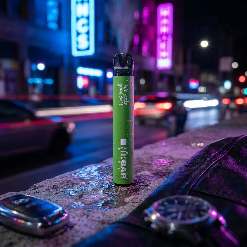 Pod descartavel NikBar Plus Spearmint apoiado em parapeito urbano com luzes neon azuis e magenta ao fundo - Vapor Gringo