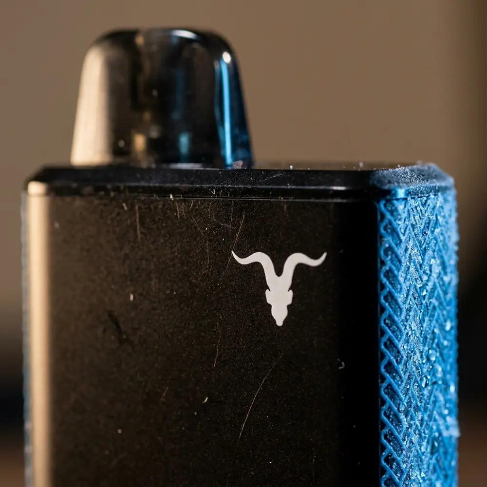 Macro do Pod Descartavel V60 Ignite Blue Razz Ice mostrando logo, textura e gotas de condensacao - Vapor Gringo
