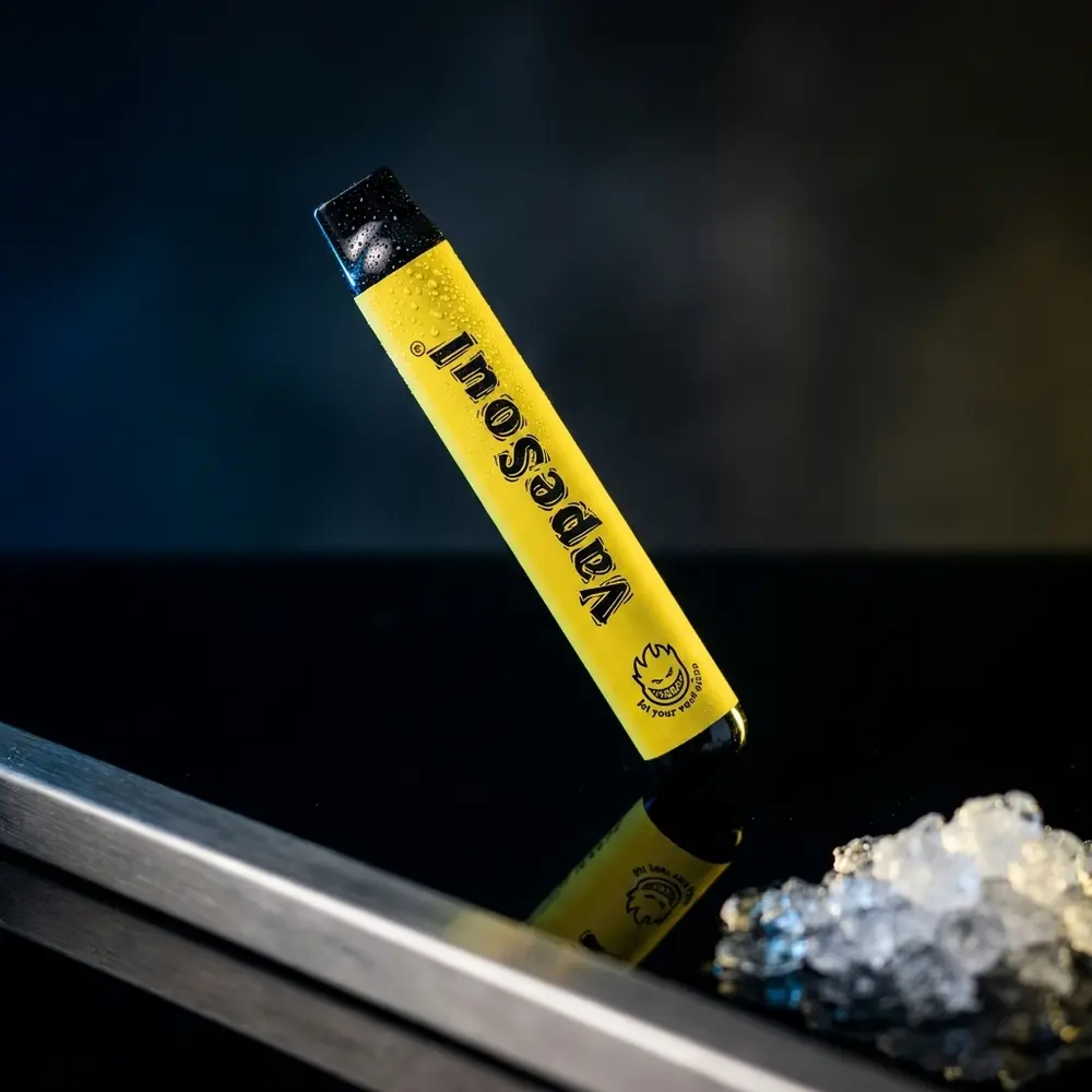 Pod descartavel Vapesoul Banana Ice em superficie acrilica preta com reflexos frios e luz amarela - Vapor Gringo