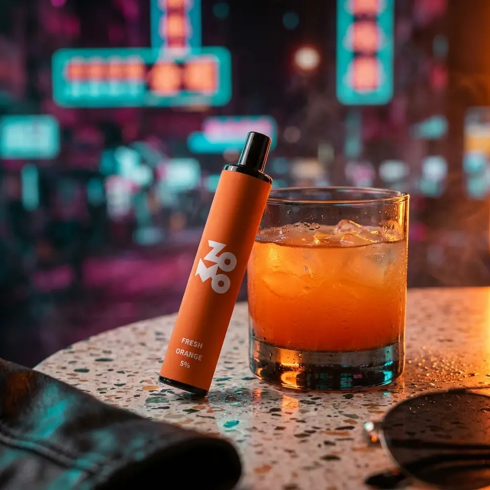 Pod Zomo Flow Fresh Orange encostado em copo com coquetel laranja, mesa terrazzo e neon urbano ao fundo - Vapor Gringo