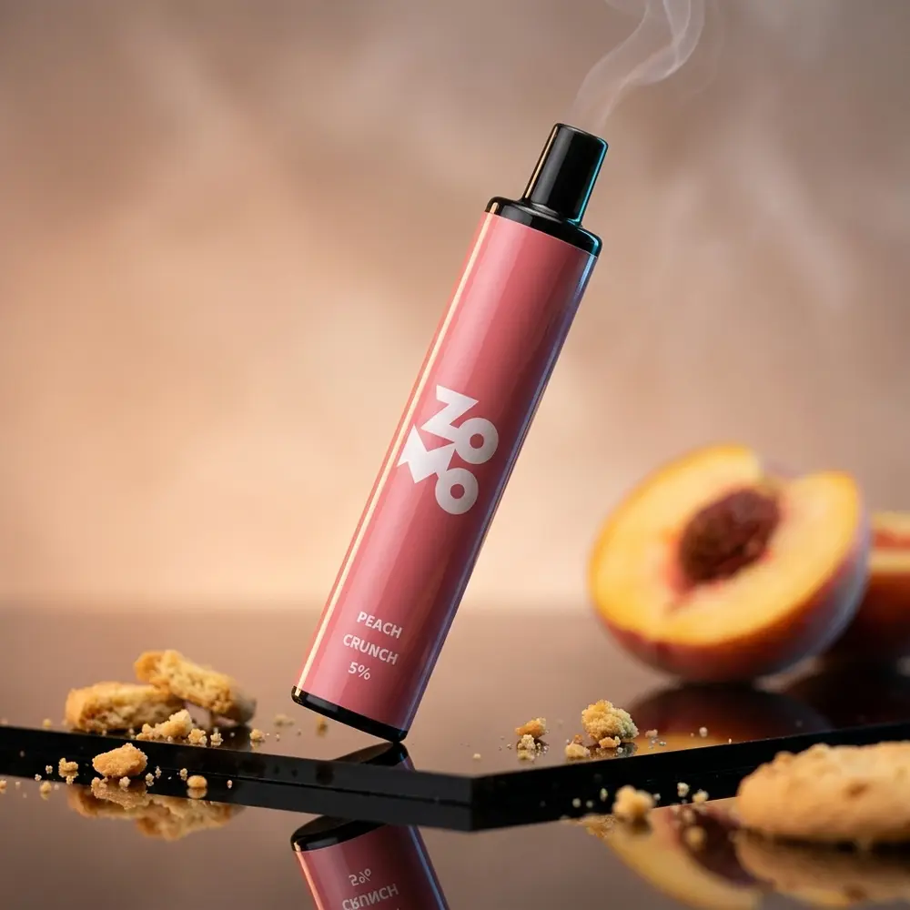 Pod Descartável Zomo Flow Peach Crunch sobre acrílico preto com reflexos dourados e pedaços de bolacha ao fundo - Vapor Gringo