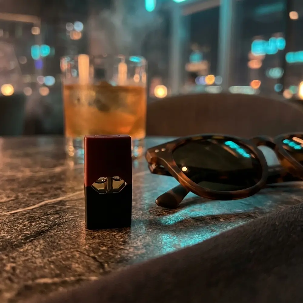Cartucho Pod Juul Tabaco Virginia sobre mesa de lounge em mármore e couro, luzes neon desfocadas ao fundo - Vapor Gringo