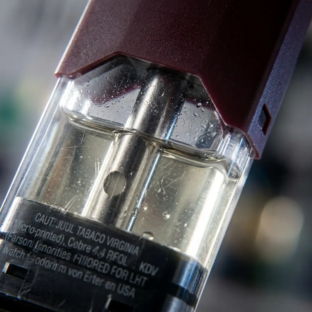 Macro do cartucho Pod Juul Tabaco Virginia mostrando bocal metálico, câmara transparente e gotas de condensação - Vapor Gringo