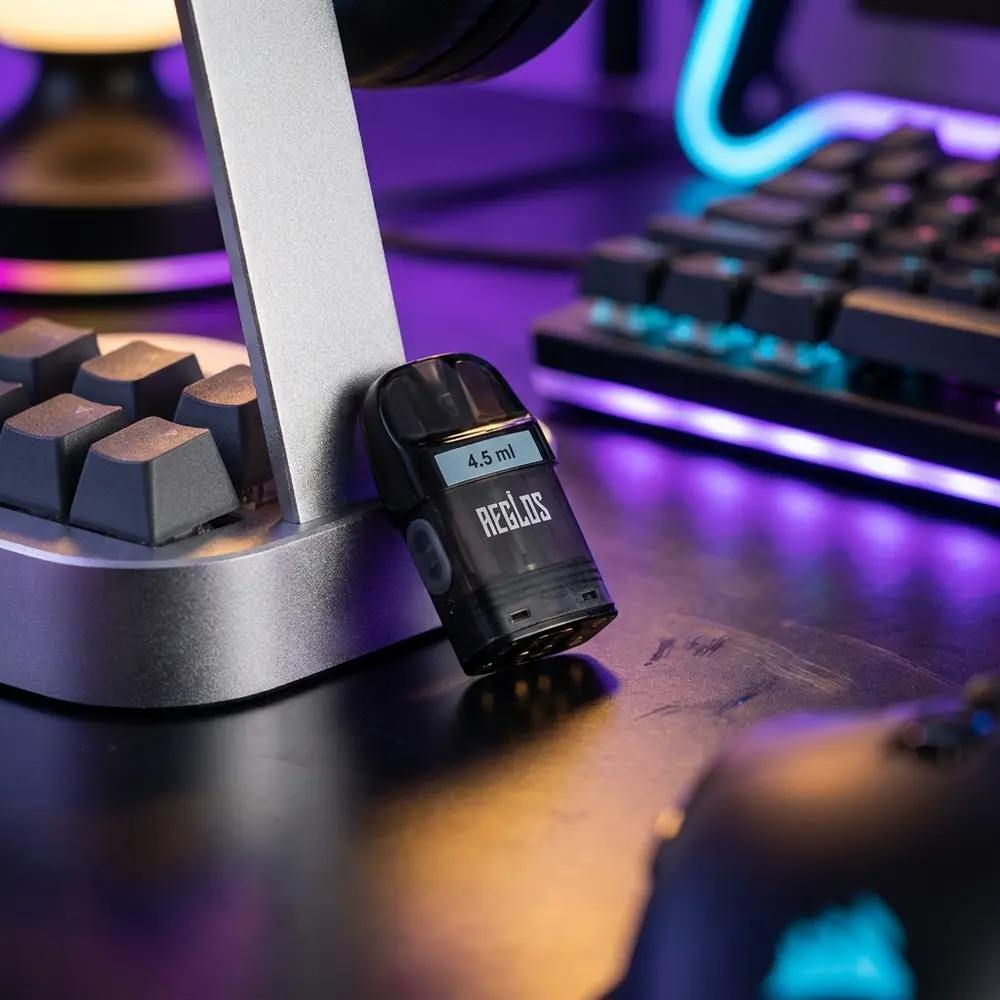 Pod Reposição Aeglos H2 Uwell apoiado em mesa gamer RGB ao lado de teclado mecânico e luzes desfocadas - Vapor Gringo