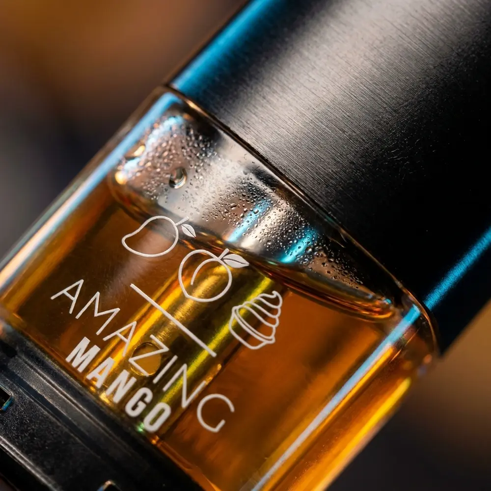 Close-up do pod reposicao Amazing Mango Naked100, concha transparente, secao metalica e gotas de condensacao - Vapor Gringo
