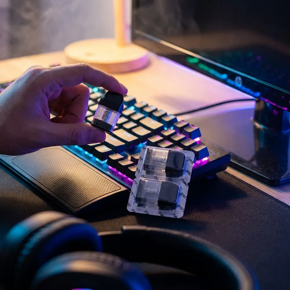 Pod Uwell Caliburn G sobre mesa gamer com teclado RGB ao fundo e mão segurando para escala - Vapor Gringo