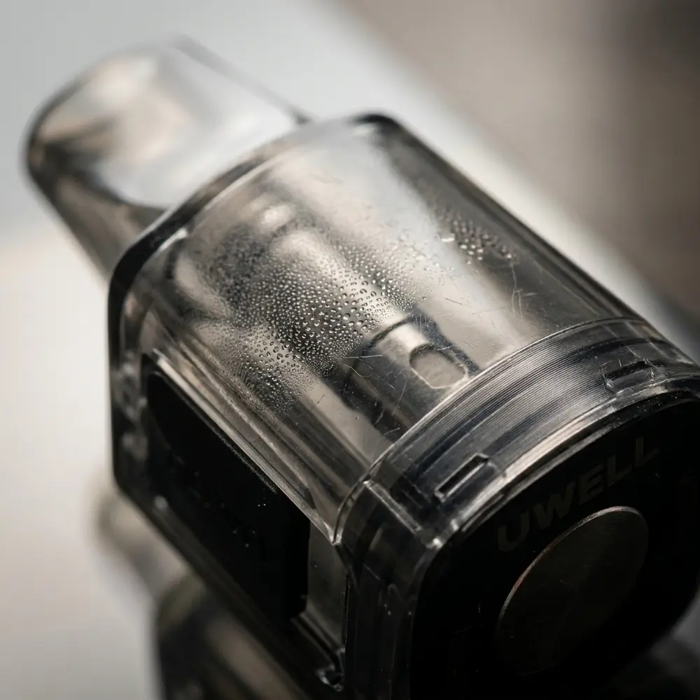 Close-up do Pod Reposição Caliburn Ironfist L Uwell mostrando bocal, conector metálico e gotas na carcaça transparente - Vapor Gringo