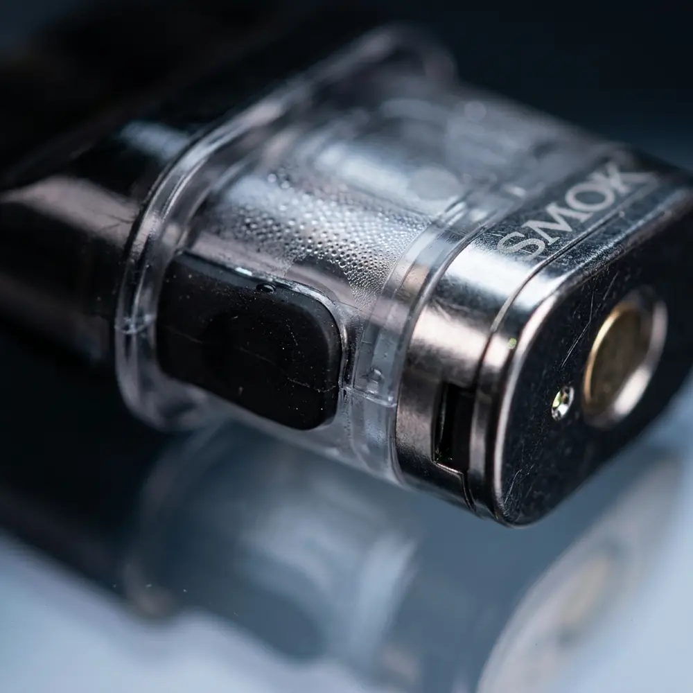 Detalhe macro do Pod Novo 4 mostrando tampa de silicone, contatos metálicos e gotículas internas - Vapor Gringo