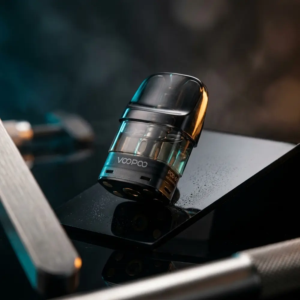 Pod de reposicao VooPoo POD-S1 apoiado em base acrilica preta brilhante, iluminacao azul e ambar e reflexos metalicos visiveis - Vapor Gringo