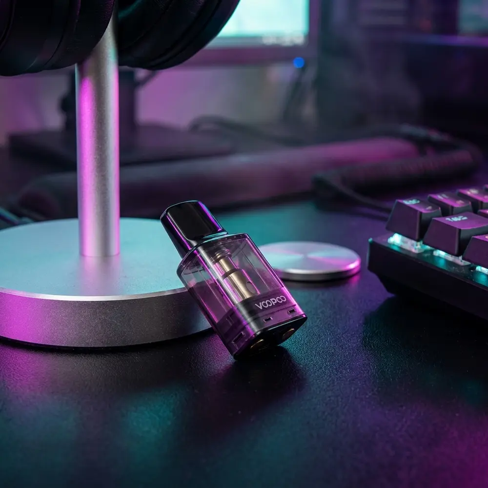 Pod VooPoo POD-S1 sobre mesa gamer RGB, luzes coloridas refletindo no plastico transparente e contatos metalicos visiveis - Vapor Gringo