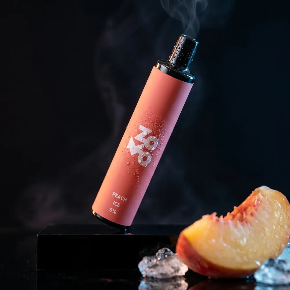 Pod Descartável Zomo Flow Peach Ice sobre acrílico preto com gotas e fatia de pêssego desfocada - Vapor Gringo