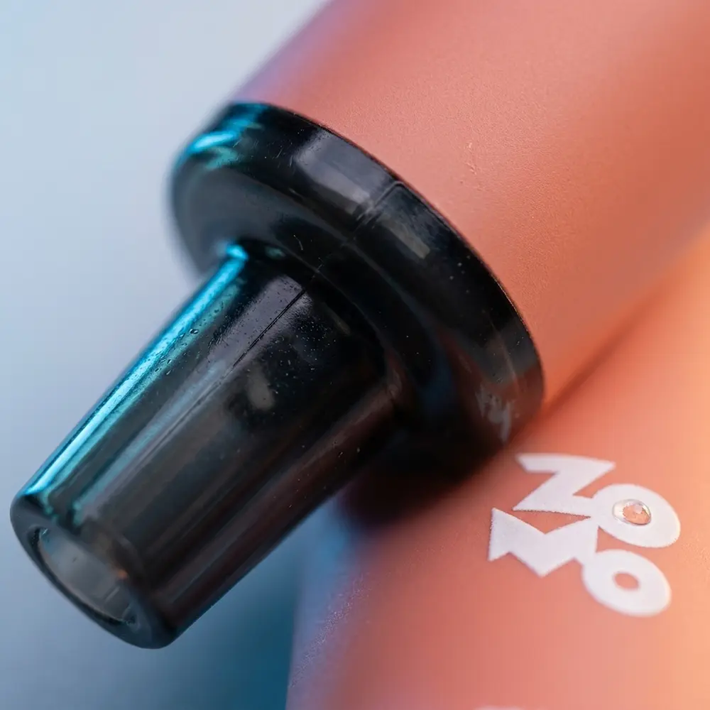 Close-up do bocal e rótulo do Pod Zomo Flow Peach Ice com gotículas e reflexos metálicos - Vapor Gringo