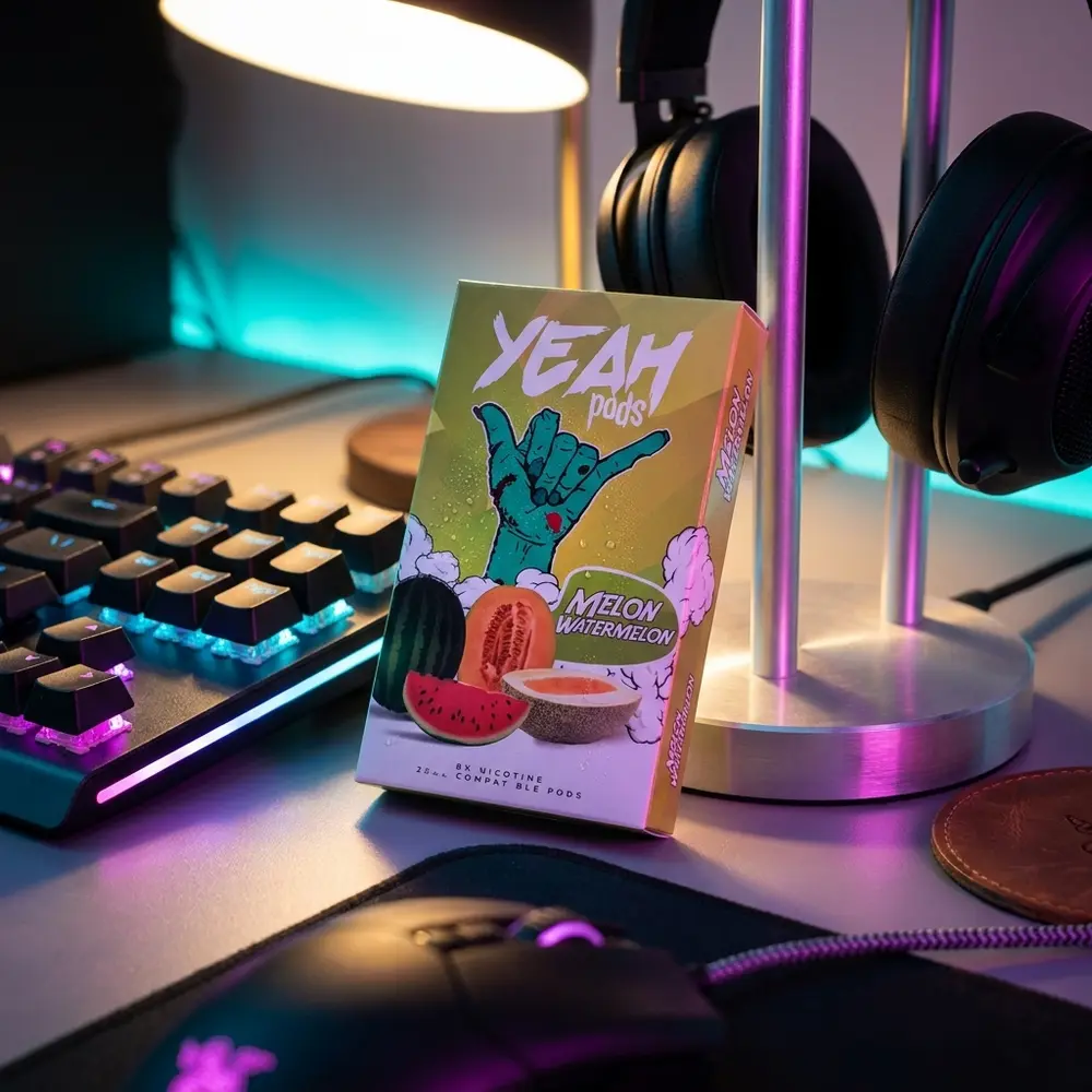 refil para pod juul yeah melon watermelon apoiado em mesa gamer rgb, reflexos neon e objetos de lifestyle ao redor - Vapor Gringo