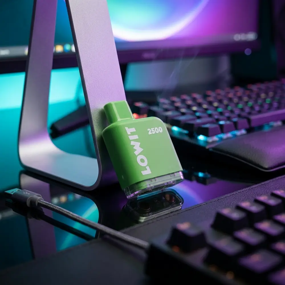 Refil Pod Lowit 2500 em setup gamer RGB apoiado no suporte de fones, teclado desfocado ao fundo - Vapor Gringo