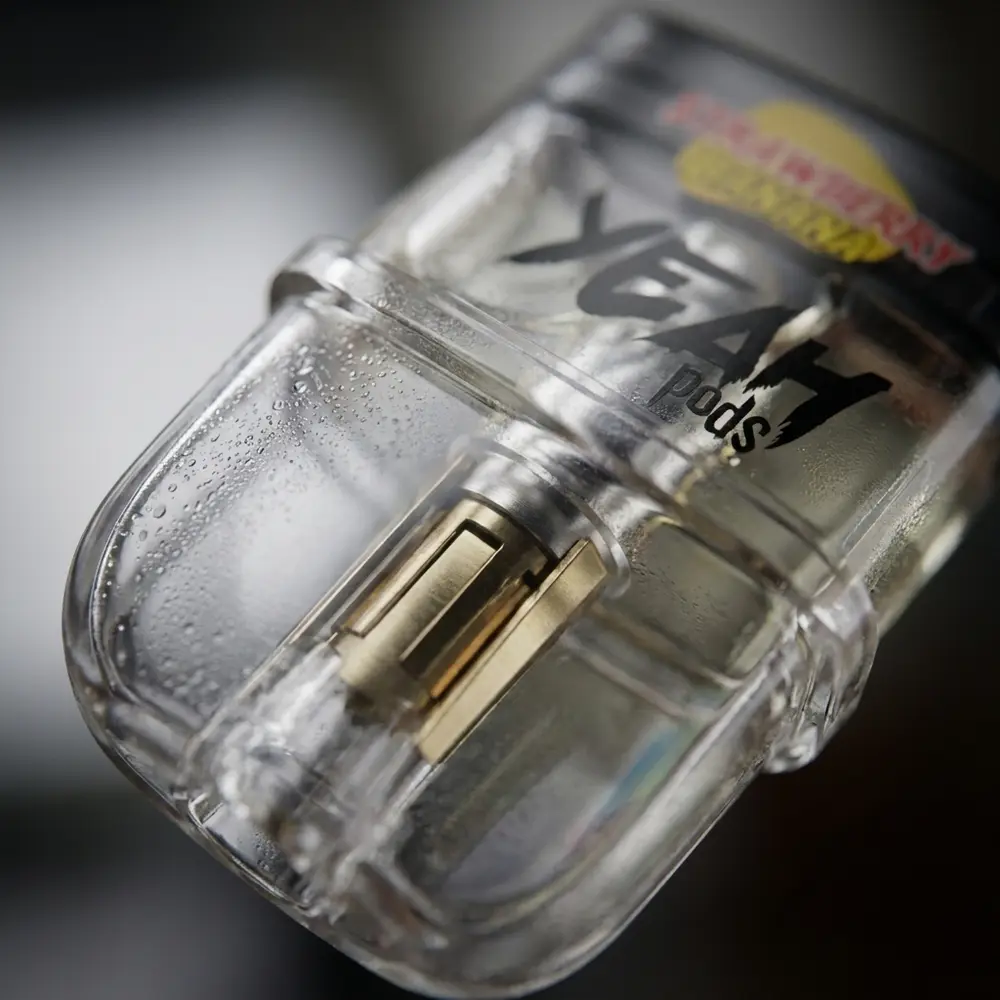 Close-up do refil Pod Juul Yeah Strawberry Banana mostrando invólucro transparente, contatos metálicos e gotas. - Vapor Gringo