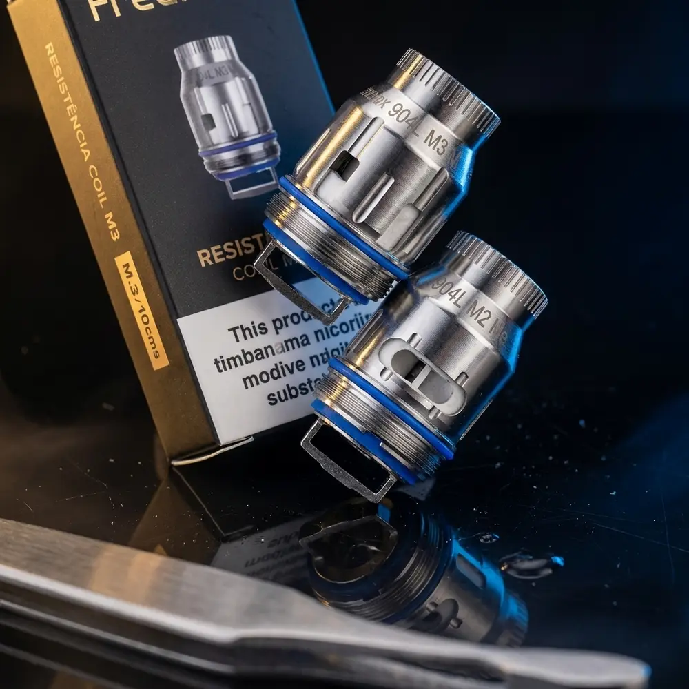 Resistência Coil 904L M Freemax sobre acrílico preto com luzes douradas e azuis e reflexos intensos - Vapor Gringo
