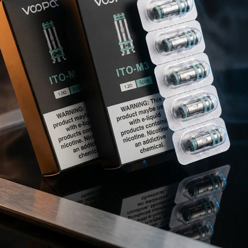 Resistência Coil ITO Voopoo em close sobre acrílico preto com reflexos âmbar e azul, embalagem visível - Vapor Gringo