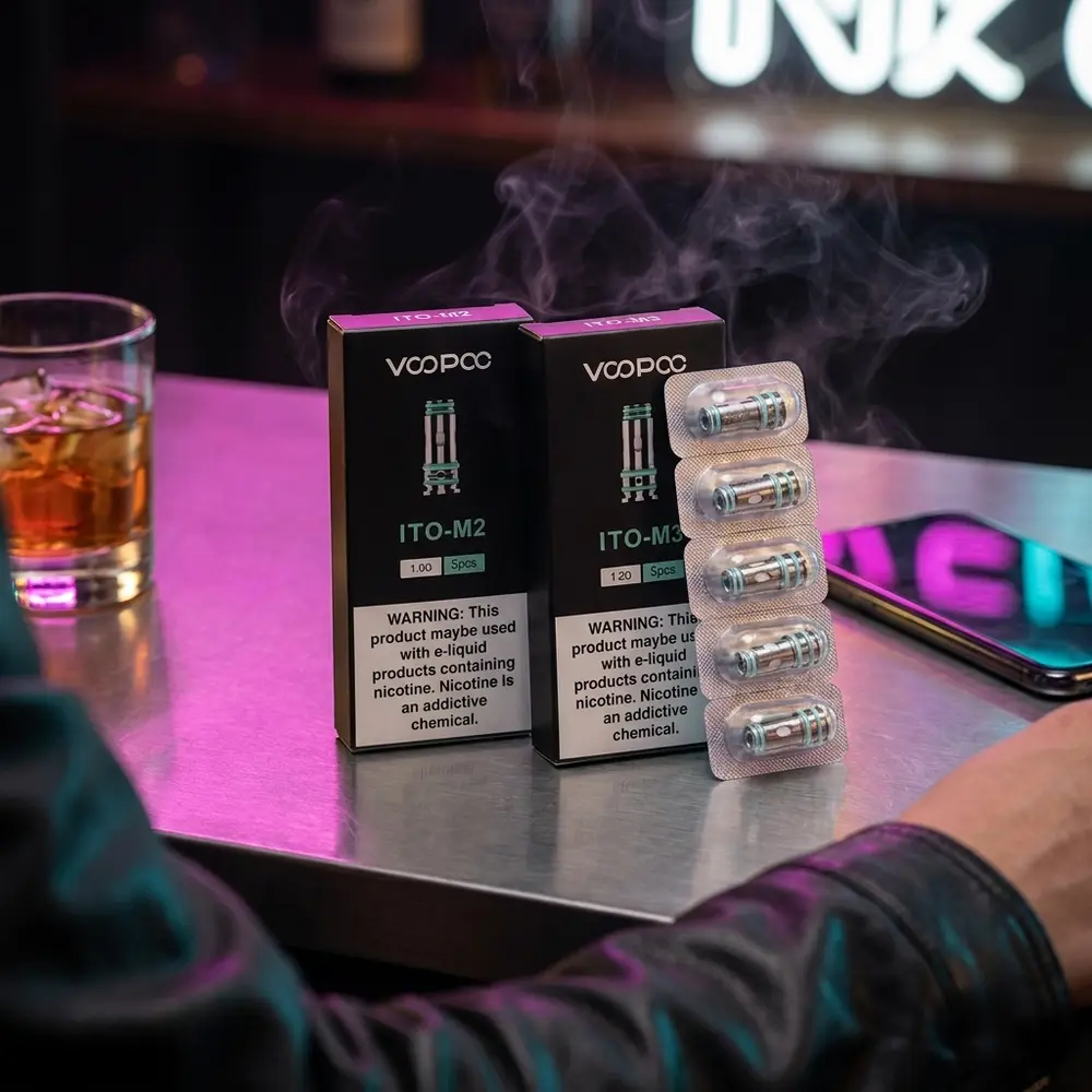 Resistência Coil ITO Voopoo apoiada em balcão metálico com luzes neon ao fundo e smartphone RGB desfocado - Vapor Gringo