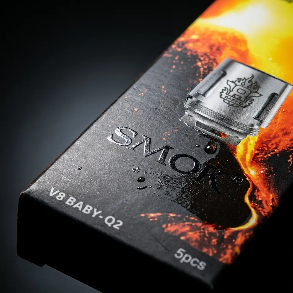 Close-up da embalagem da Resistência Coil Q2 da Smok mostrando logo, textura do papel e gotas de condensação - Vapor Gringo