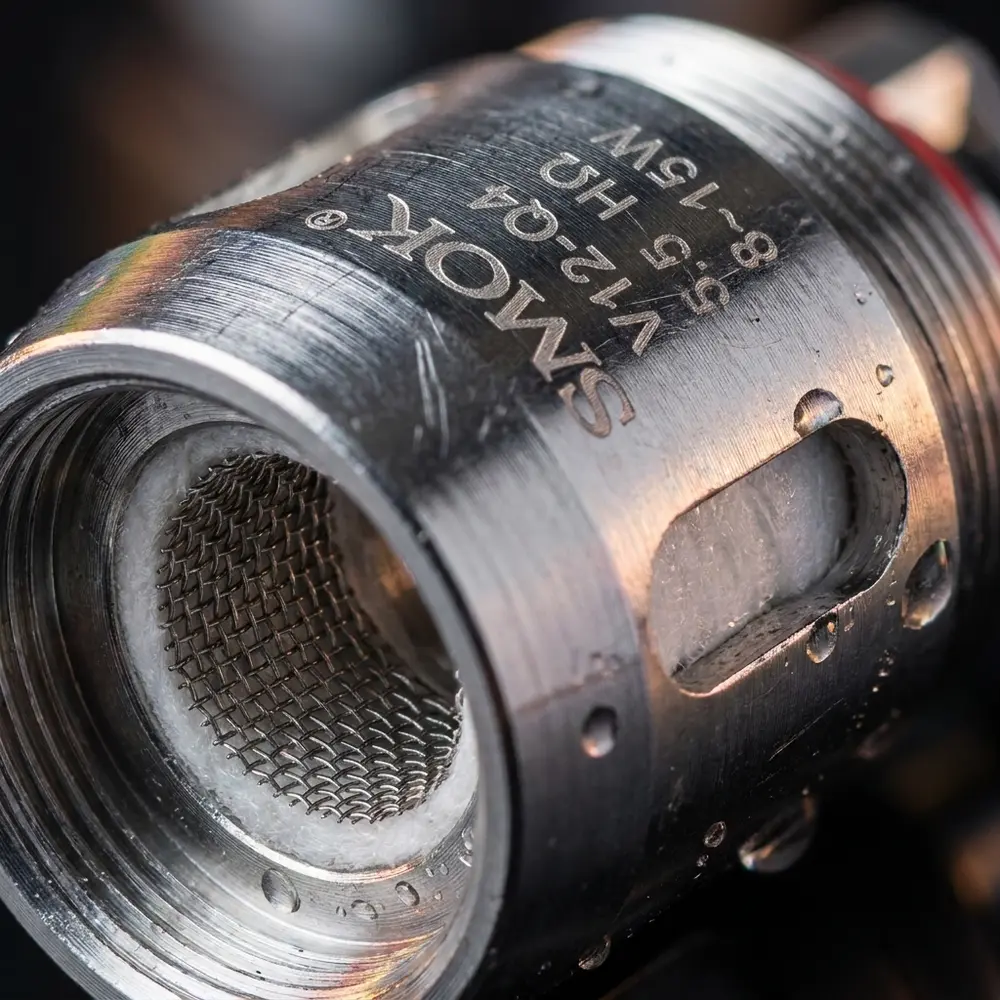 Close-up da Resistência Coil TFV12 Q4 0.15ohm mostrando malha Kanthal, marca impressa e gotas de condensação. - Vapor Gringo