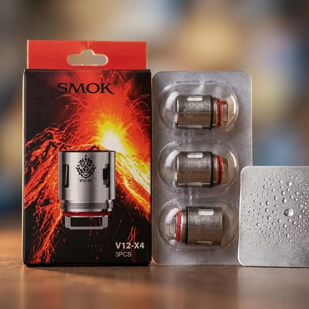 Detalhe da Resistência Coil TFV12 X4 Smok mostrando rótulo, acabamento metálico e texturas com gotas ao lado - Vapor Gringo