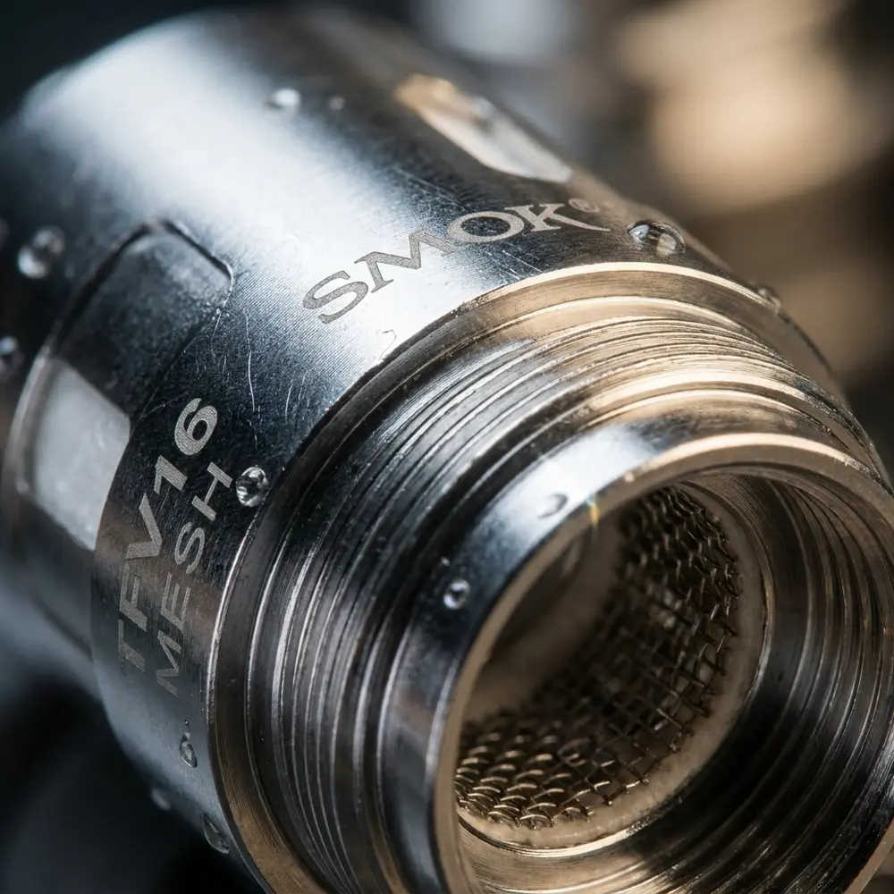 Macro da Resistência Coil TFV16 Smok mostrando textura metálica, logo gravado e gotas sutis - Vapor Gringo