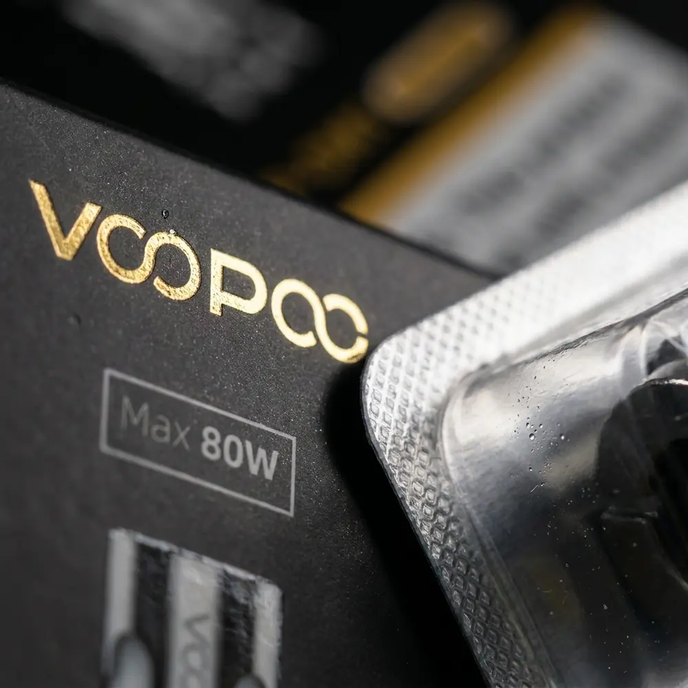 Close-up da caixa da resistencia Voopoo TPP-DM1 0,15Ω mostrando textura do papel, verniz e reflexos metalicos - Vapor Gringo