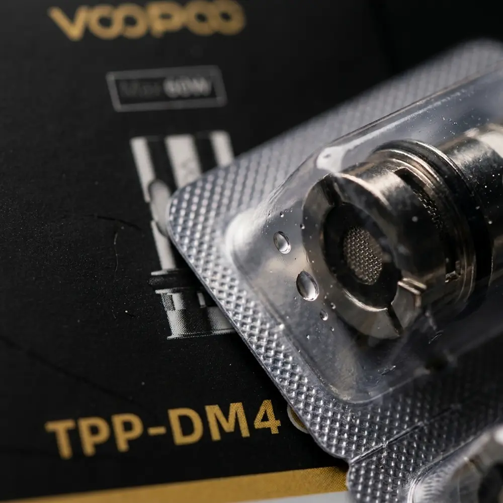 Macro da embalagem e logo Voopoo do coil TPP-DM4, textura do carton, reflexos metalicos e gotas - Vapor Gringo