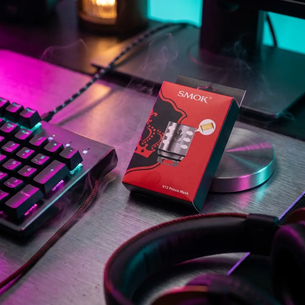 Resistência Mesh para TFV12 Prince da Smok sobre mesa RGB de gaming, com teclado e fones ao fundo e reflexos coloridos. - Vapor Gringo