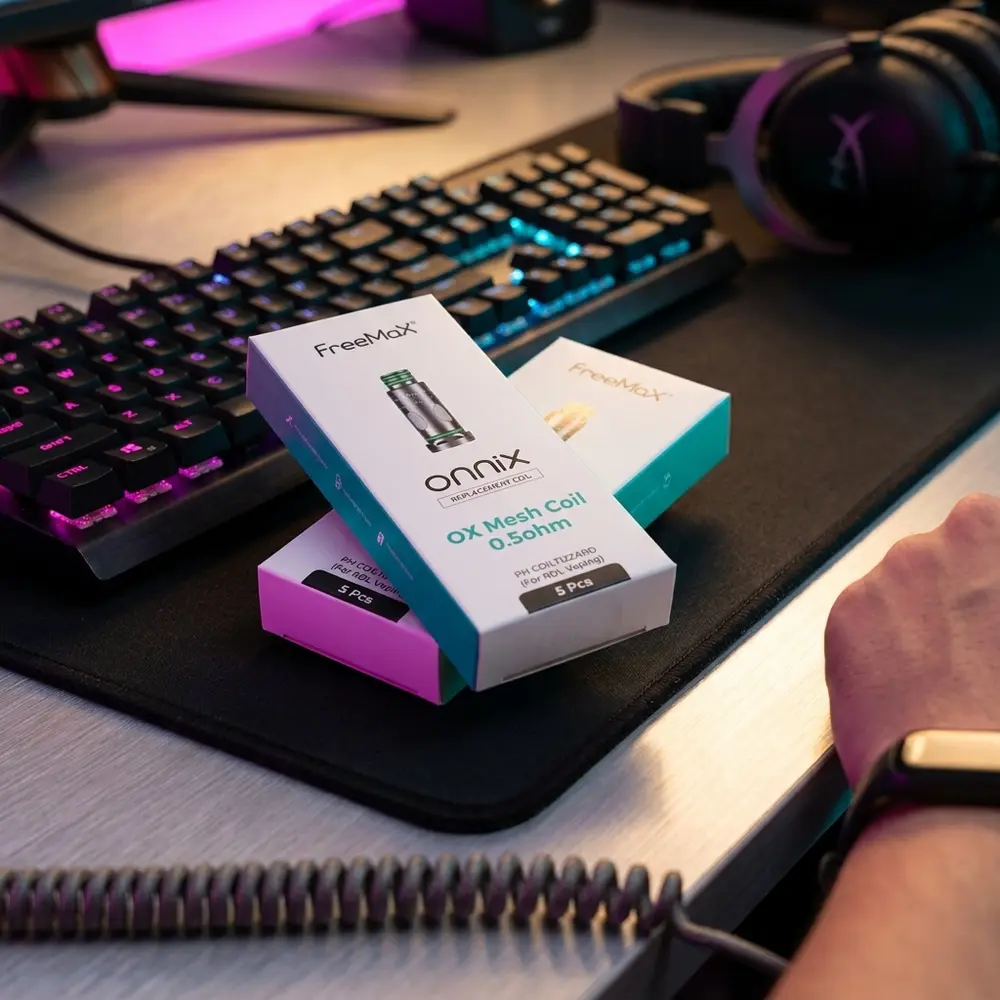 Resistência OX Mesh 0.5 ohm Freemax sobre mesa gaming com teclado desfocado e luzes RGB coloridas - Vapor Gringo