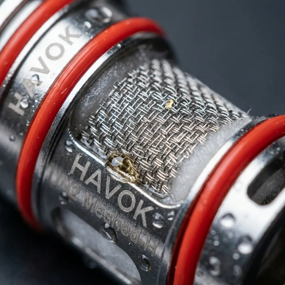 Macro da malha e marcação da Resistência UN2 Meshed Uwell mostrando textura do metal, fibras do algodão e gotas minúsculas - Vapor Gringo