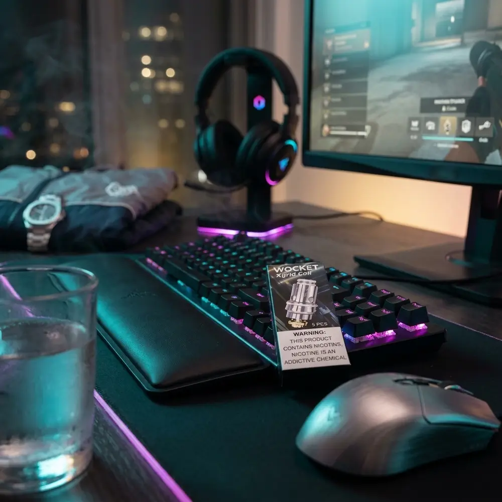 Pack da resistencia X-Grid 0.7ohm Wocket SnowWolf apoiado em mesa gamer RGB entre fones e teclado mecanico - Vapor Gringo