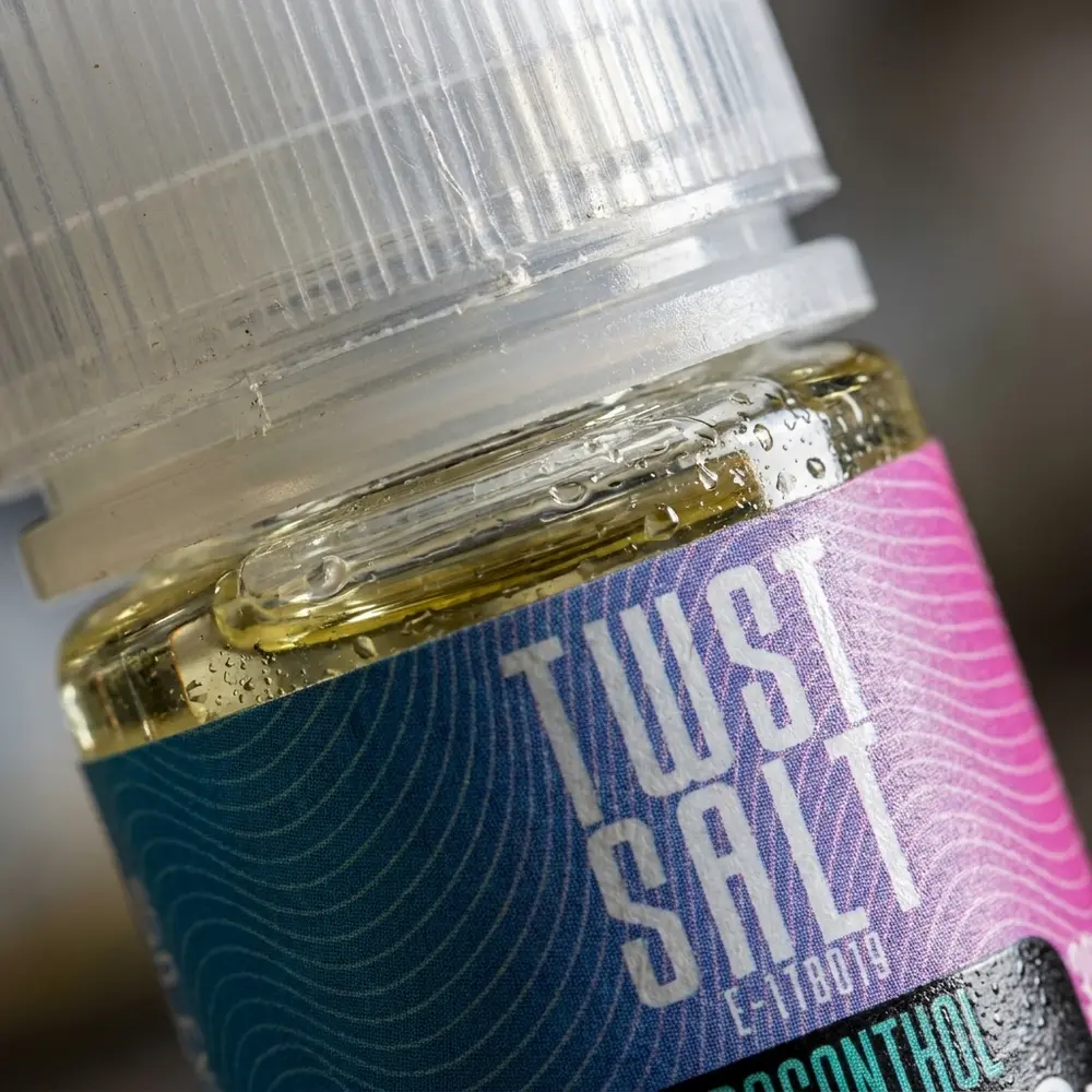 Close-up do frasco Twst Dragonthol 30ml mostrando rótulo, textura do vidro, gotas de condensacao e reflexos metalicos - Vapor Gringo