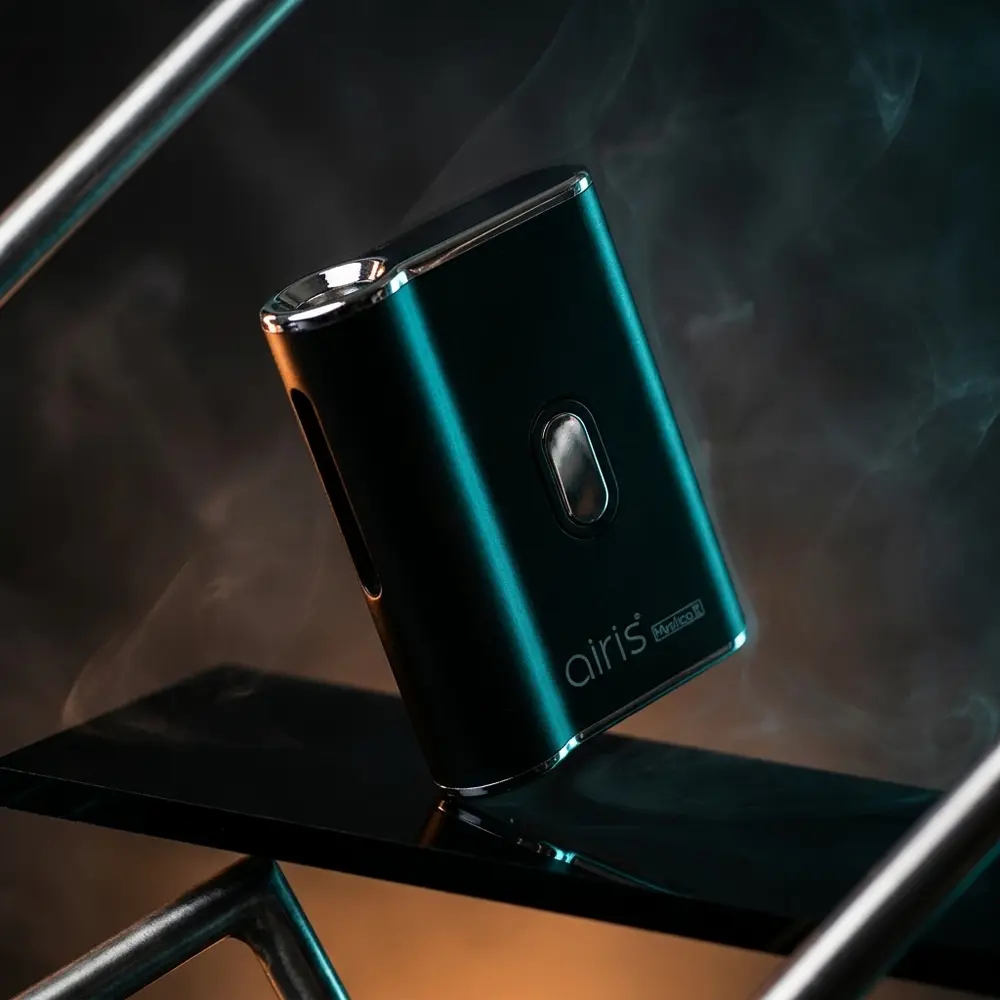 Vaporizador Mystica II Airistech preto sobre base acrilica refletiva com iluminacao dramática e leve haze - Vapor Gringo