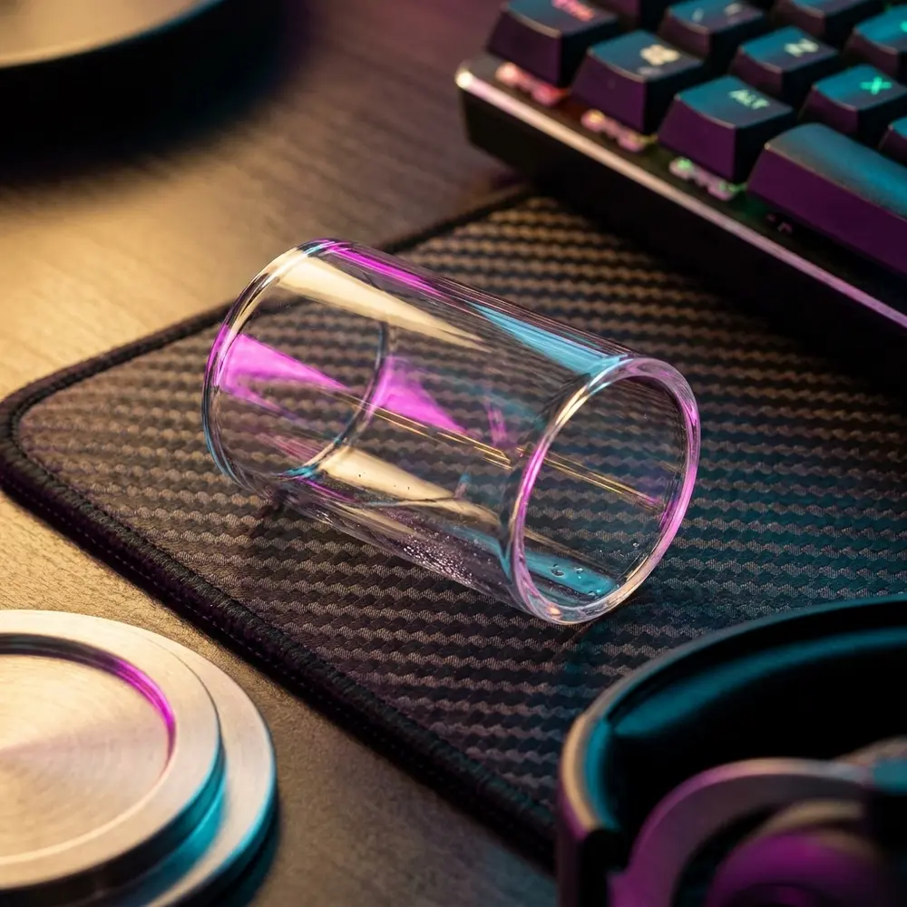 Vidro de reposição reto Dejavu RDTA 2ml sobre mousepad em setup RGB, reflexos coloridos e teclado ao fundo - Vapor Gringo