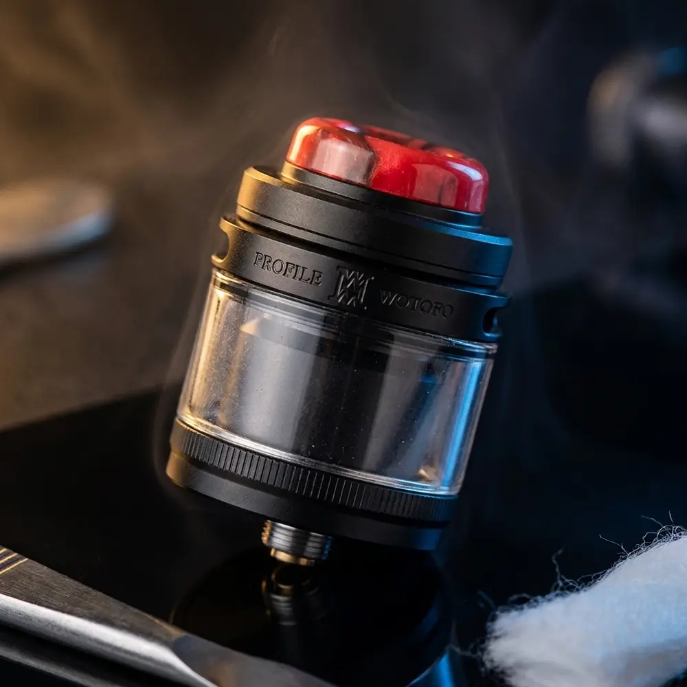 Atomizador Wotofo Profile M RTA apoiado em acrilico preto com luzes douradas e azuis, close-up premium - Vapor Gringo