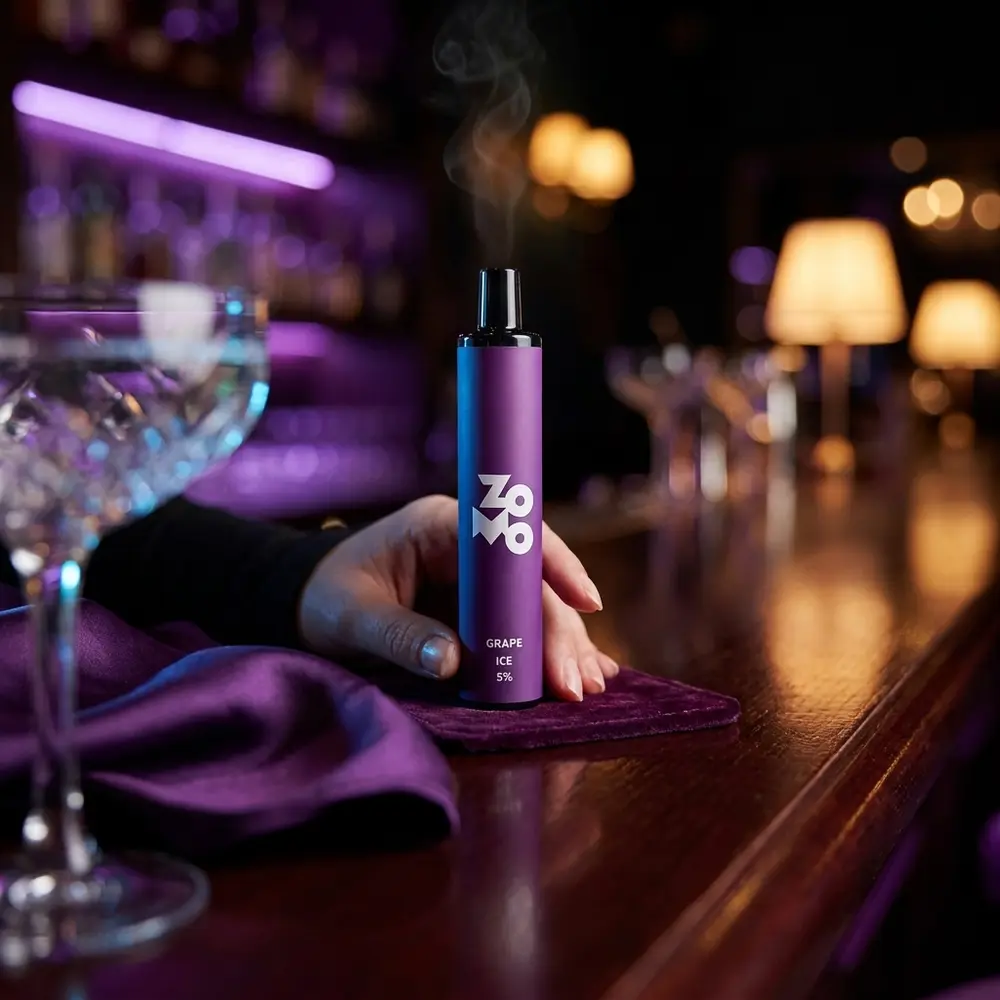 Zomo Flow Grape Ice apoiado em balcão de lounge luxuoso, luzes roxas, copo desfocado e tecido aveludado ao redor - Vapor Gringo