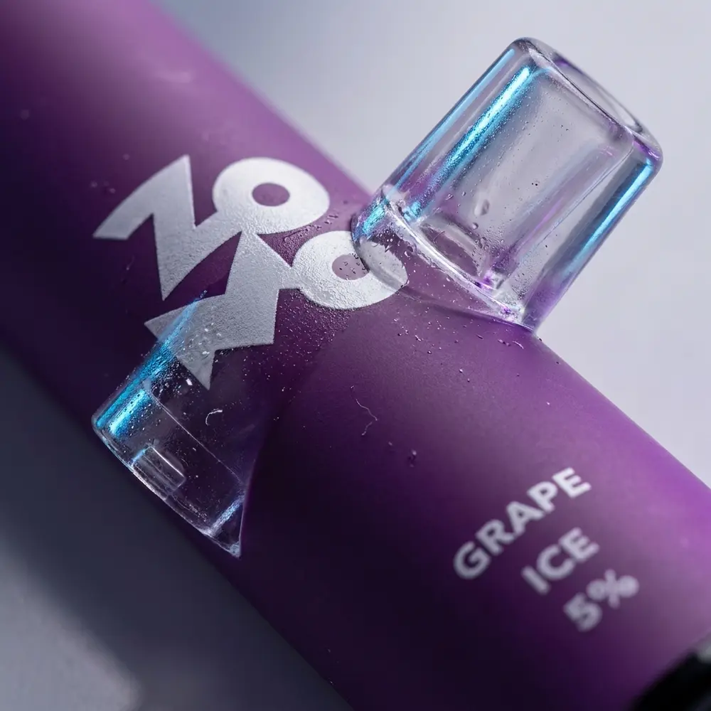 Macro do Zomo Flow Grape Ice mostrando boca, rótulo, textura, gotas de condensação e micro reflexos roxos - Vapor Gringo
