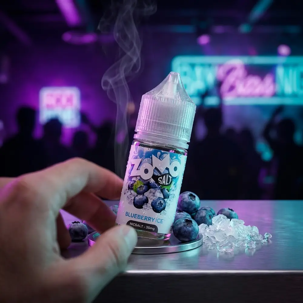 Frasco Zomo Salt Blueberry Ice apoiado em mesa metálica de bar com blueberries e gelo, luzes neon ao fundo - Vapor Gringo
