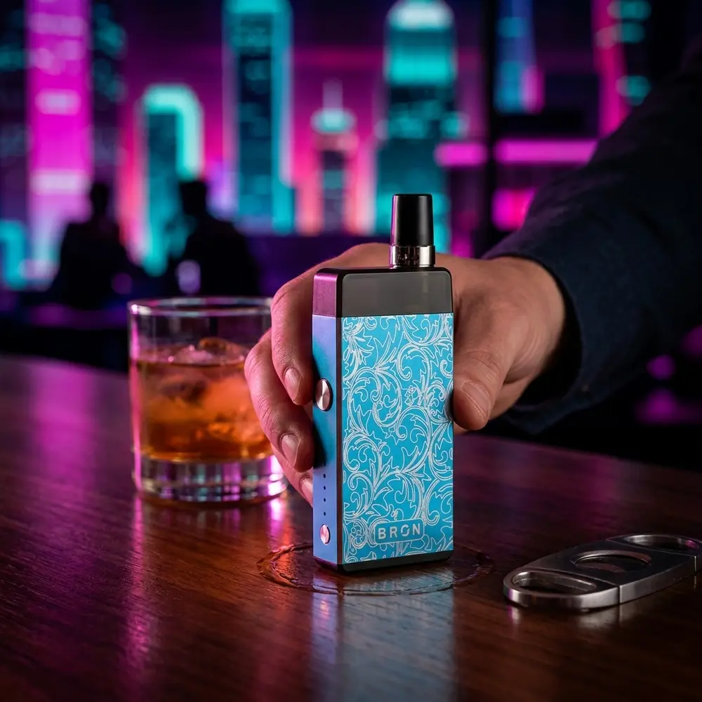 Kit Pod Bron CoilArt apoiado em balcão de bar com reflexos neon e mão segurando o aparelho - Vapor Gringo